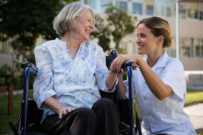 A small group of older adults and a caregiver discussing medications at a dining table with pill organizers and water glasses visible.